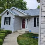 Gray vinyl-sided ranch home with black shutters and a red front door