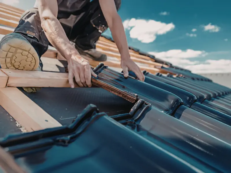 Worker's hands fitting dark blue roof tiles into place.