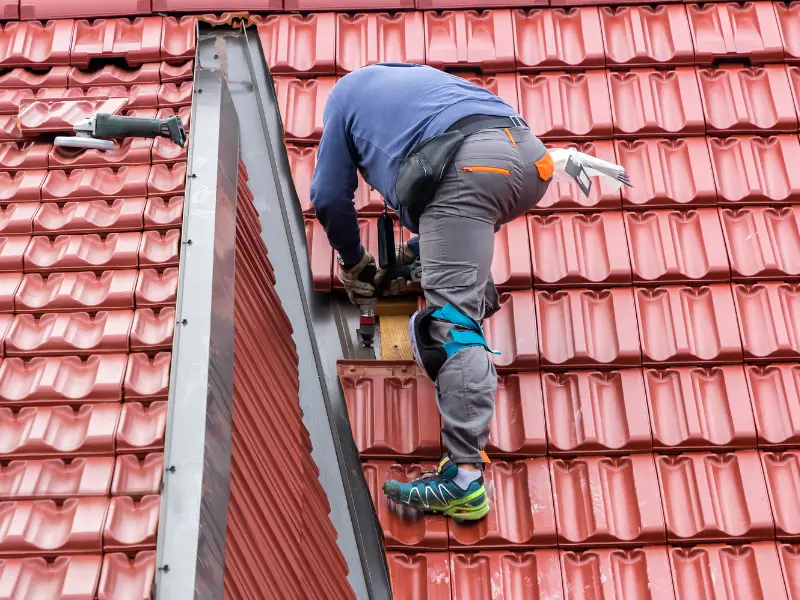 Roofer installing red tiles while balancing on a rooftop.