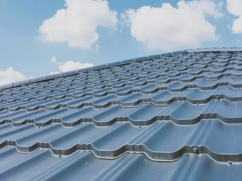 Close-up of gray metal tile roofing under a cloudy sky.