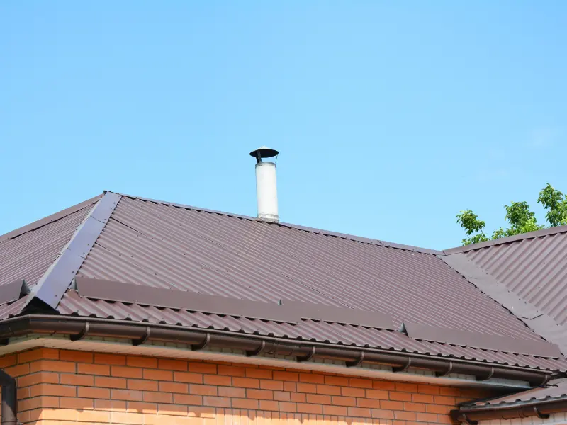Brown metal roof with chimney vent on a brick house.