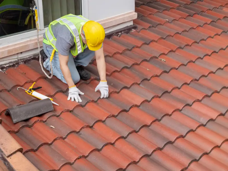 Roofer sealing red tile roof edges near a window.