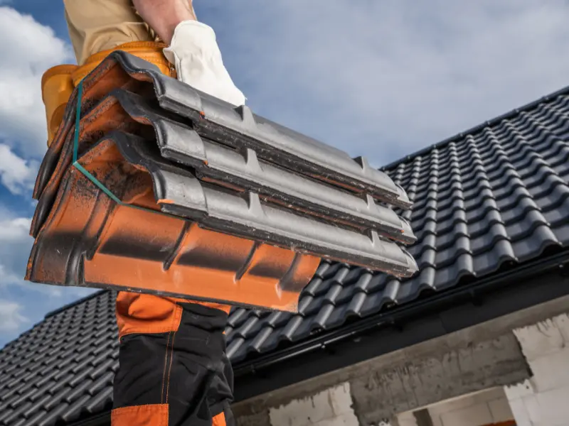 Worker carrying a stack of gray roof tiles.