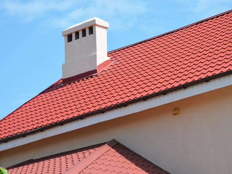 Red tile roof with a white chimney against blue sky.