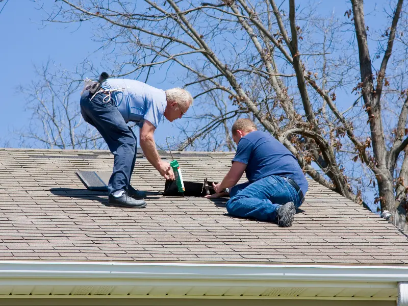 Two roofers installing a roof vent on a shingle roof.