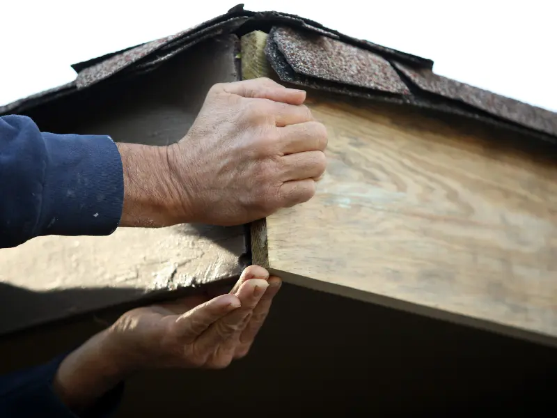 Close-up of hands nailing a shingle to a roof edge.