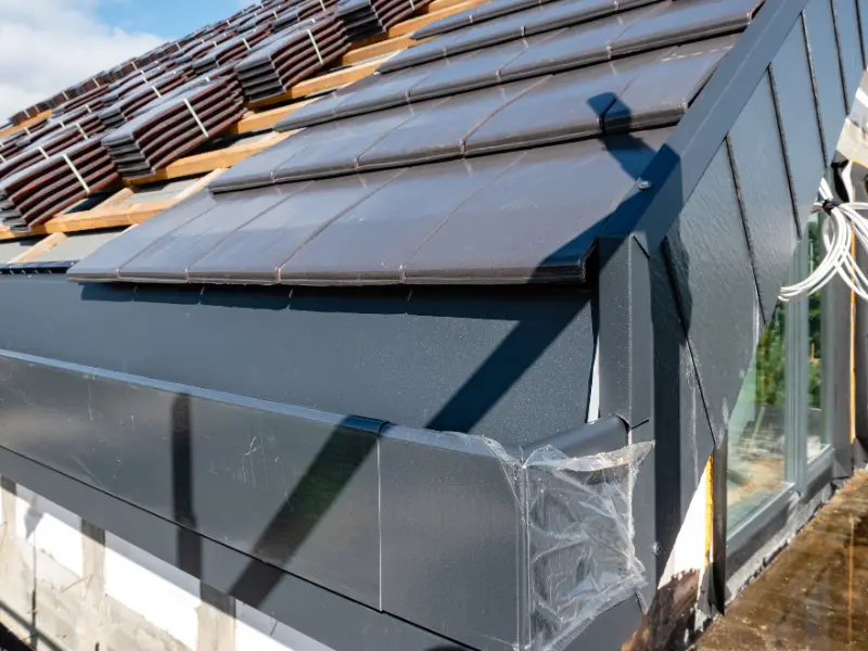 Close-up of dark tile roof and dormer flashing installation.
