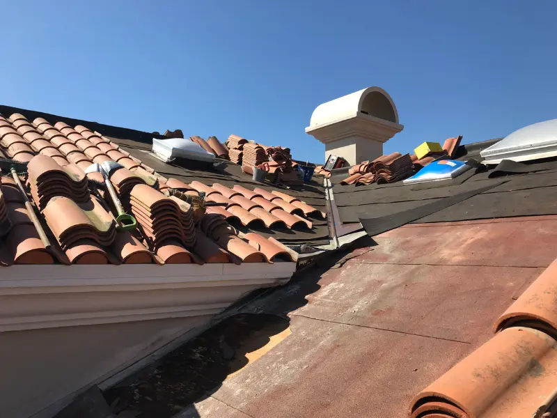 Clay tiles staged on a roof next to a chimney cap.