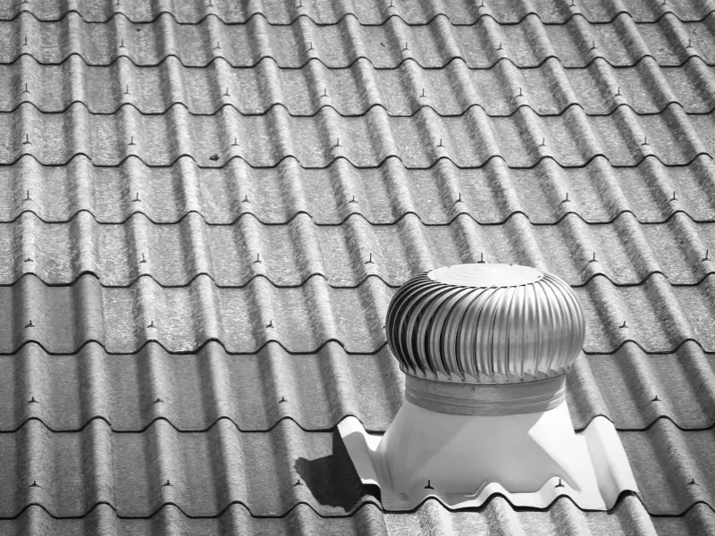Black and white close-up of a tile roof with vent turbine.