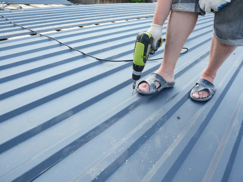 Worker drilling screws into a corrugated metal roof panel.