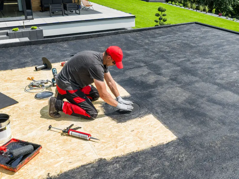 Worker installing a flat roof membrane on a modern house.