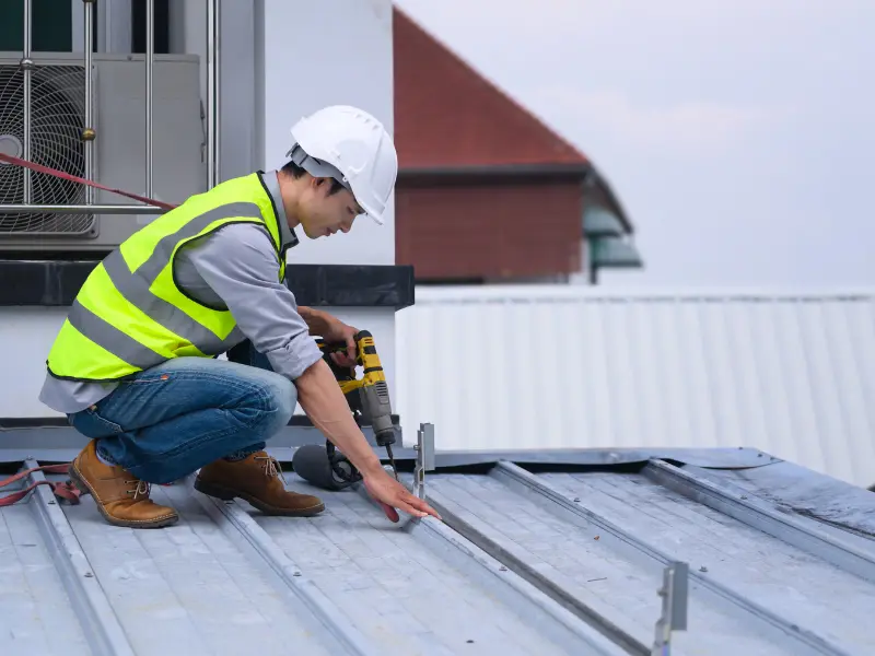 Worker installing metal roofing panels near a rooftop unit.