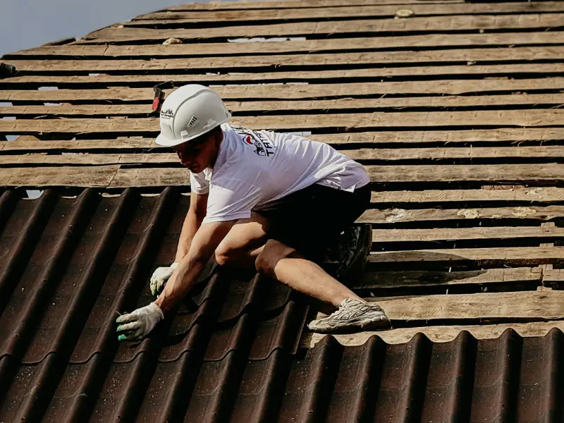 Roofer installing brown corrugated tiles on a roof deck.