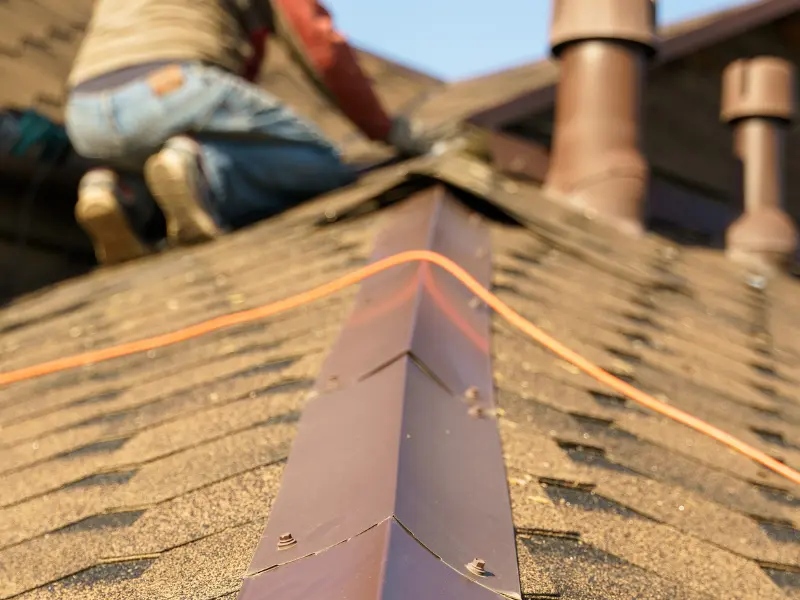 Close-up of a roof ridge cap with a worker in the background.