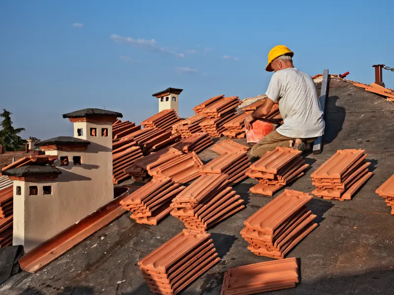 Roofer arranging stacks of terracotta roof tiles near chimneys.