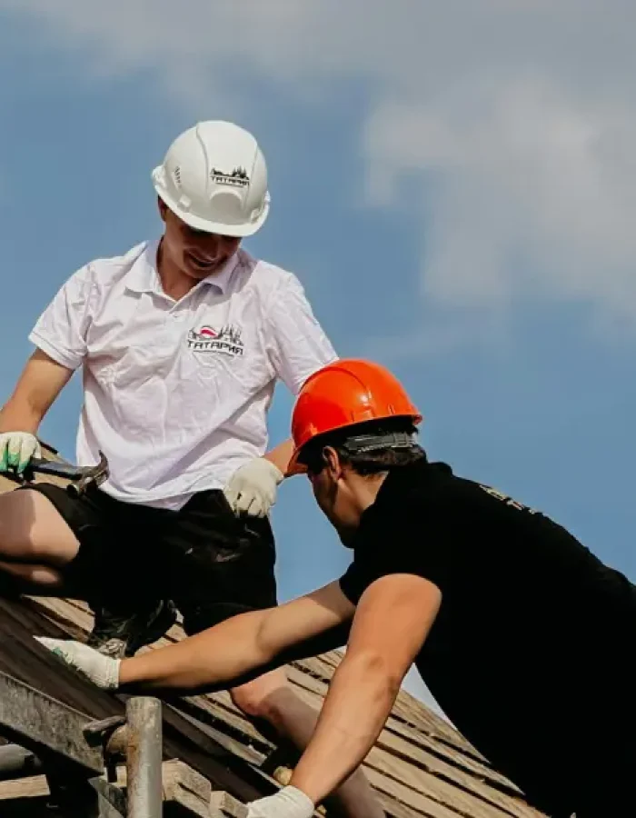 Roofing crew working together on a tiled roof against a blue sky.
