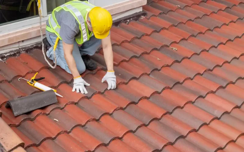 Roofer sealing red tile roof edges near a window.
