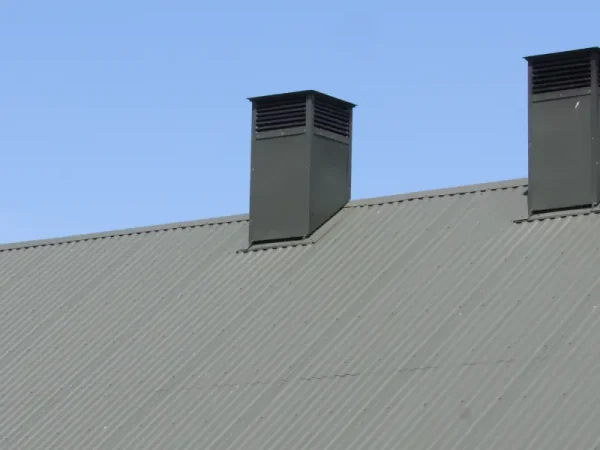 Metal roof with ventilation stacks against blue sky.