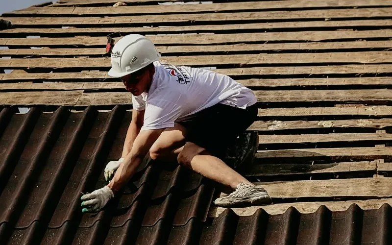 Roofer installing brown corrugated tiles on a roof deck.